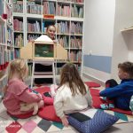 Bibliotekarka otwiera skrzynkę z teatrzykiem kamishibai, widać kilkoro uczestników