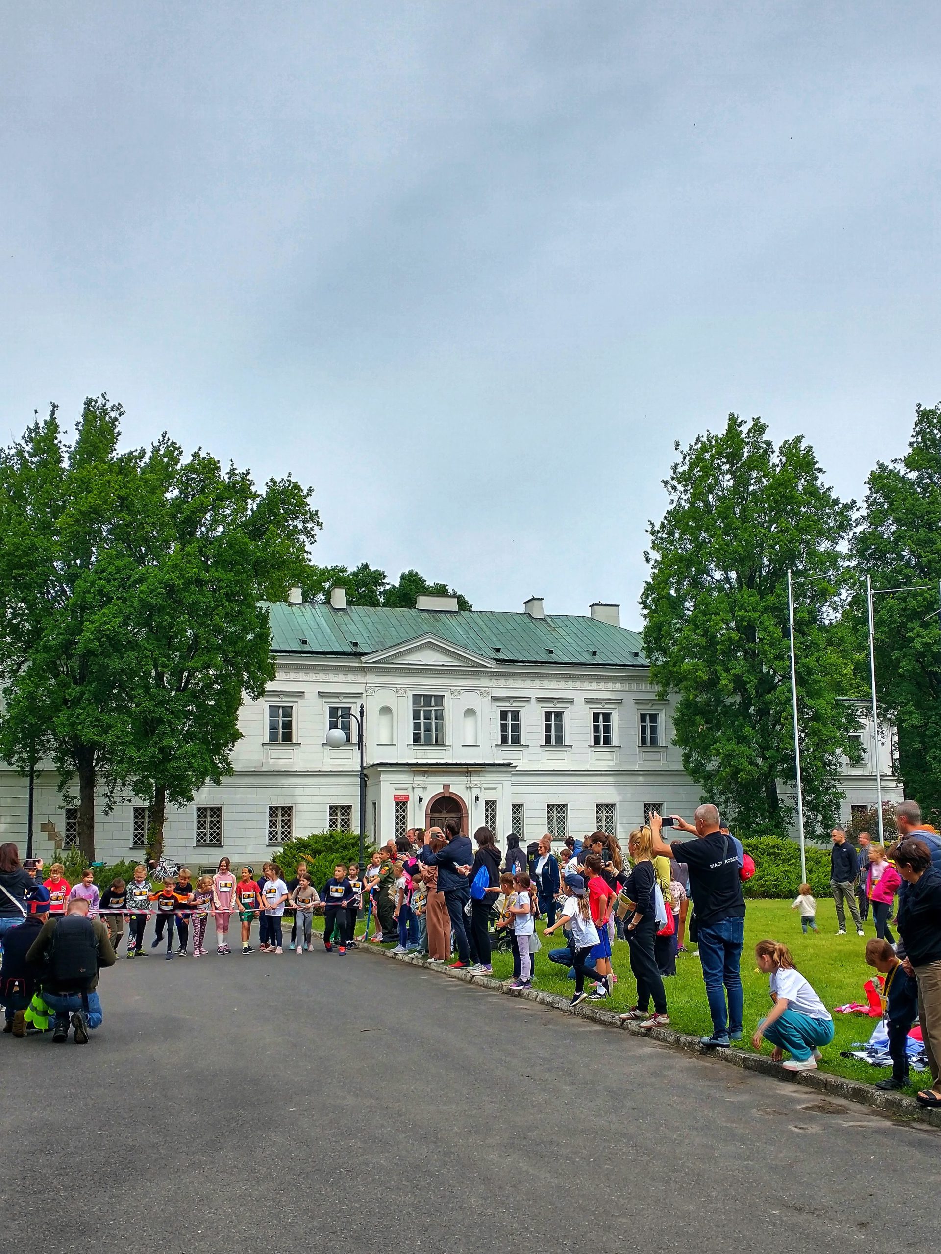 Grupa dorosłych z dziećmi podczas biegu - widać tor biegu i szykujące się do startu dzieci