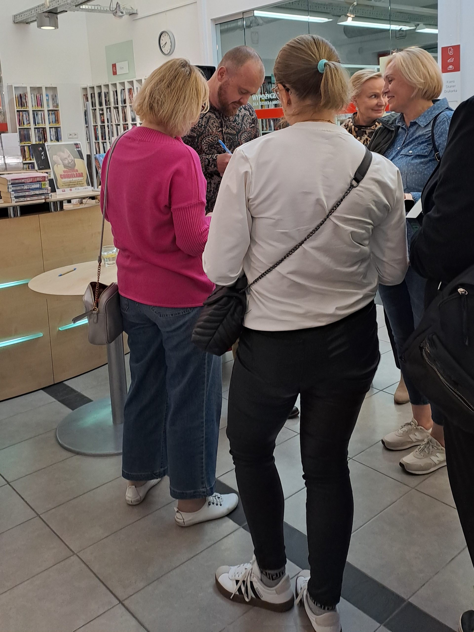 Sesja autografów z Wojciechem Chmielarzem - autor podpisuje książki, otoczony przez uczestników spotkania