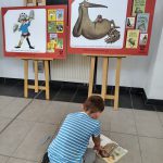 Chłopiec siedzi na podłodze przed planszą wystawy z otwartą książką