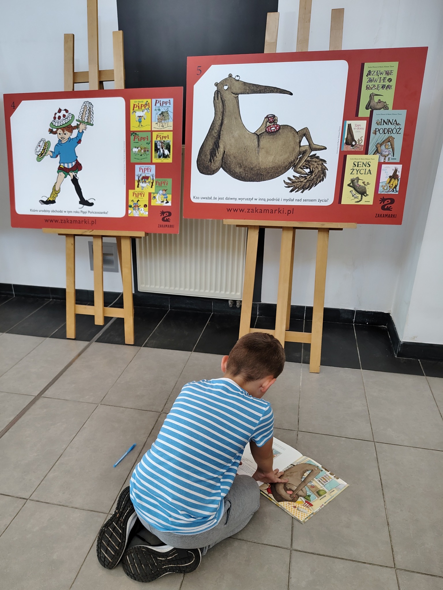 Chłopiec siedzi na podłodze przed planszą wystawy z otwartą książką
