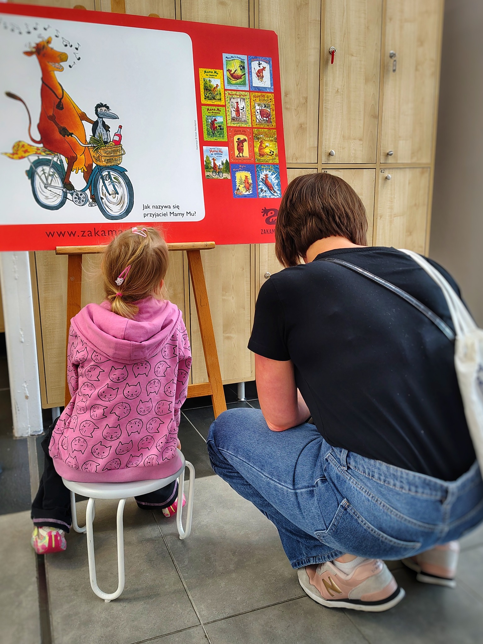 Mama z córką siedzą przed jedną z plansz wystawy, rozwiązują zadania z quizu