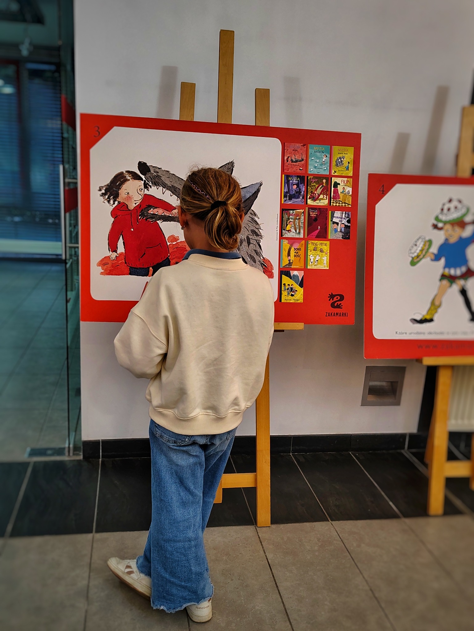 Dziewczynka stoi przed jedną z plansz wystawy w holu biblioteki