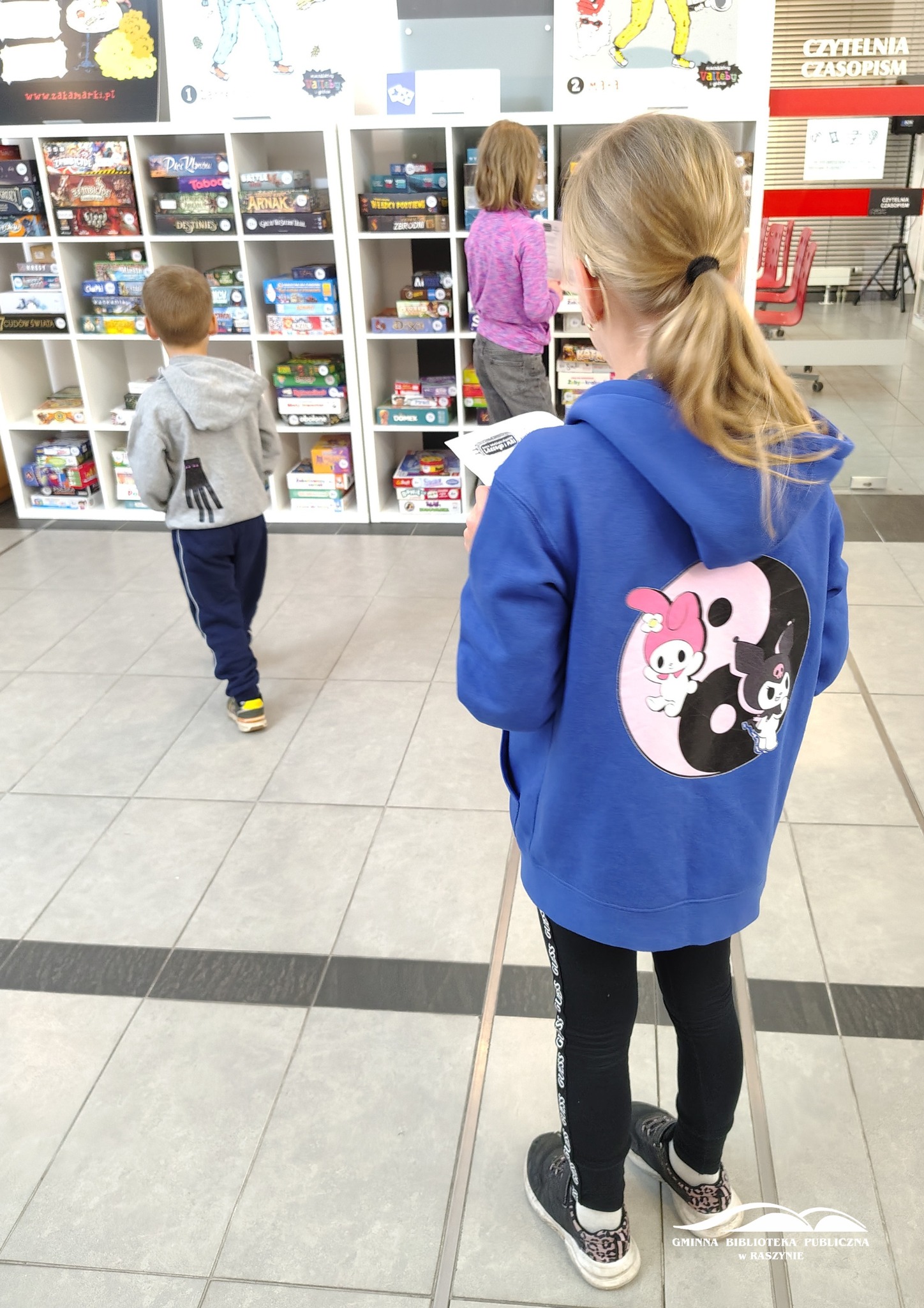 Dzieci oglądają gry planszowe na regale w holu