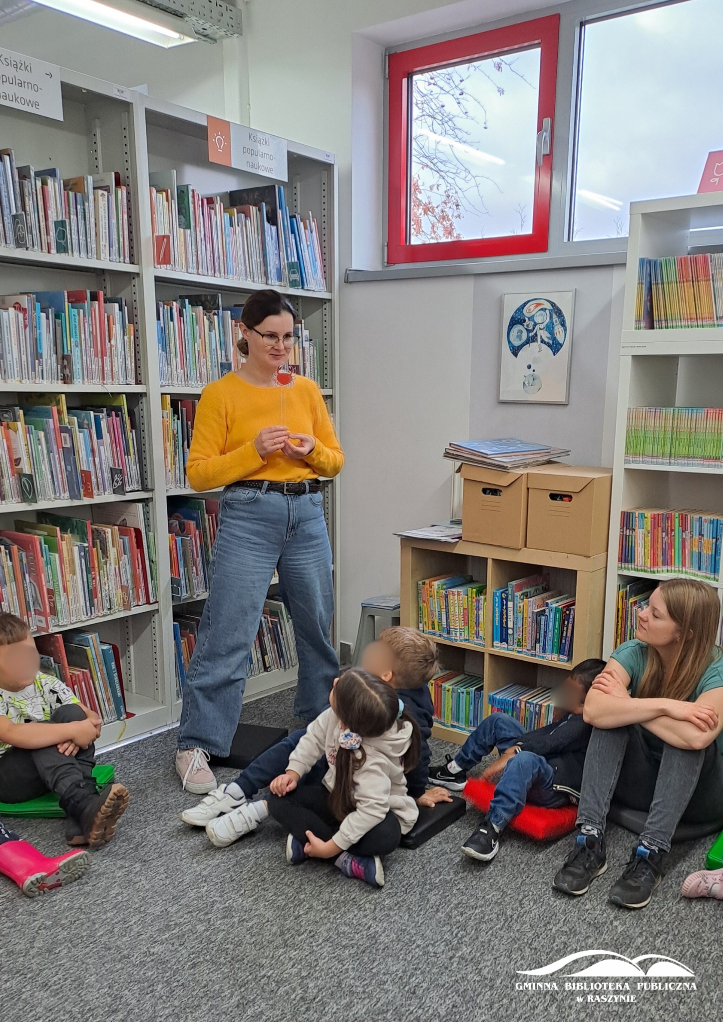 Bibliotekarka pokazuje papierowego kraba, dzieci i nauczycielka obserwują