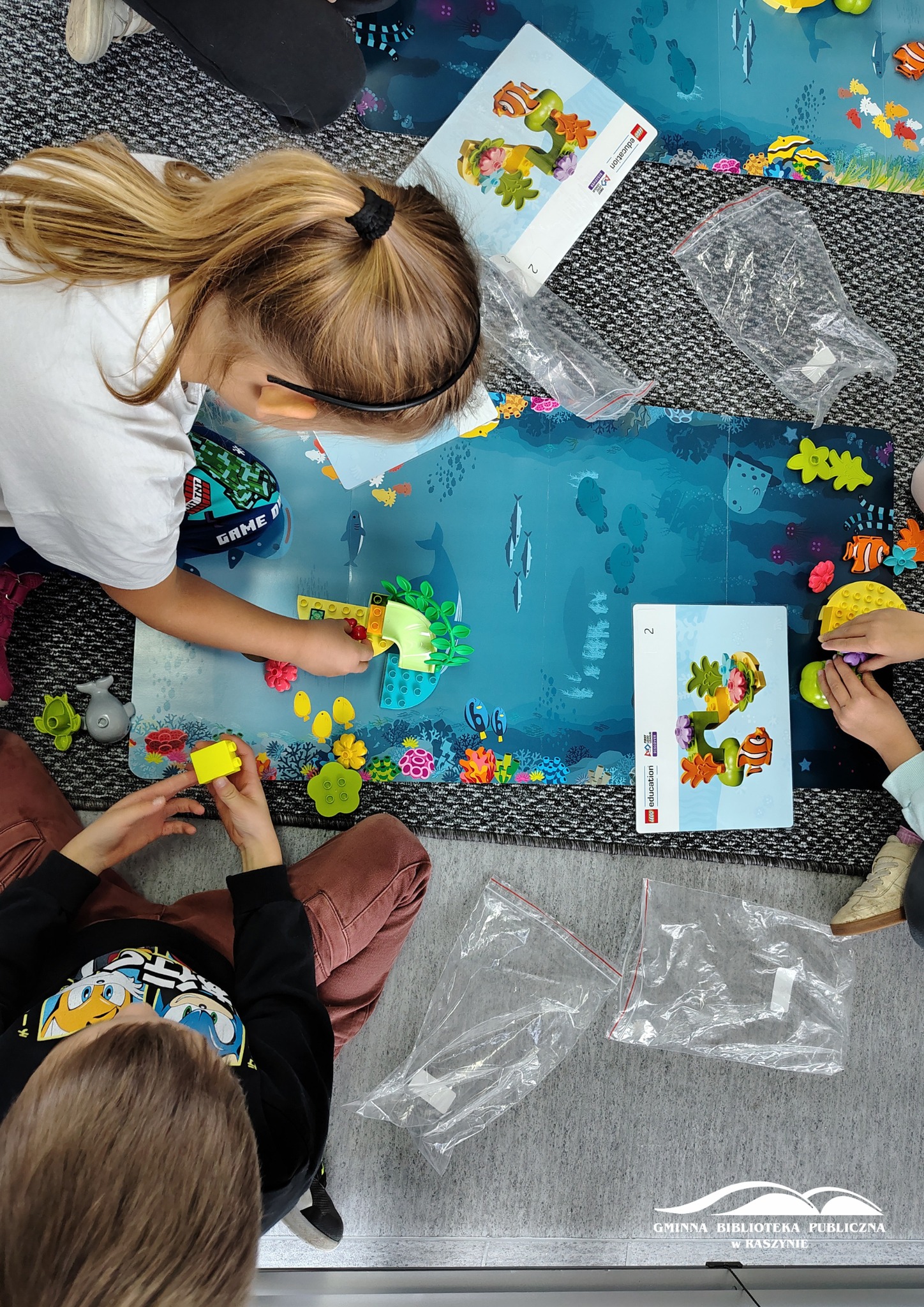 Dzieci siedzą przy planszy przedstawiającej podwodny świat, układają klocki