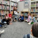 Bibliotekarka pokazuje ilustrację z książki, dzieci siedzące w koło obserwują