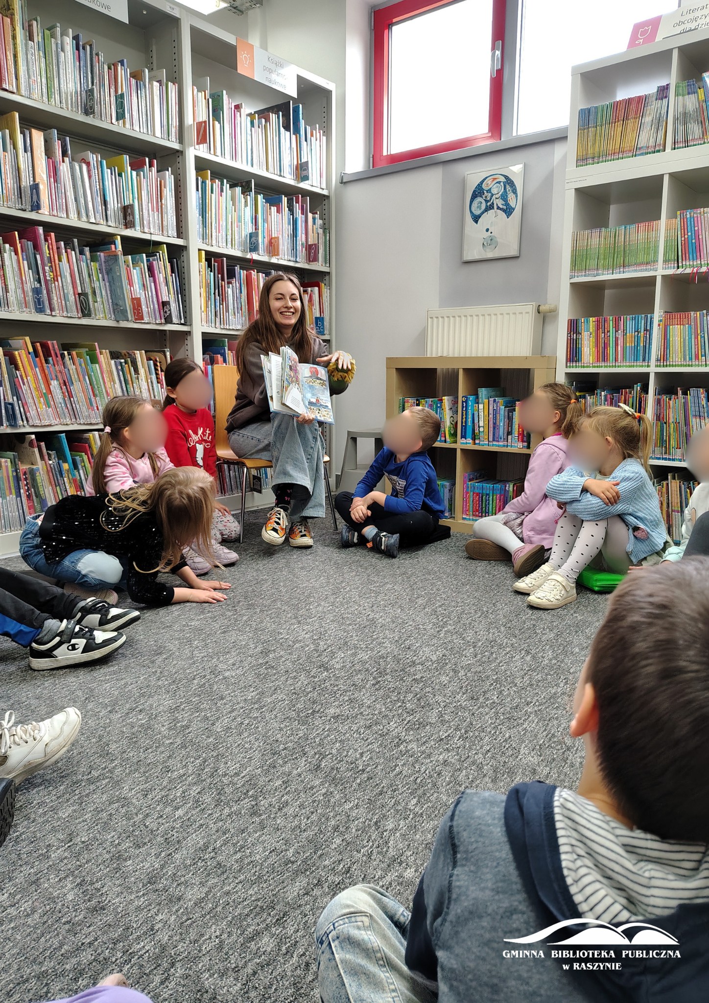 Bibliotekarka pokazuje ilustrację z książki, dzieci siedzące w koło obserwują