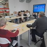 Grupa uczestników zajęć z obsługi smartfona - prowadzący tłumaczy