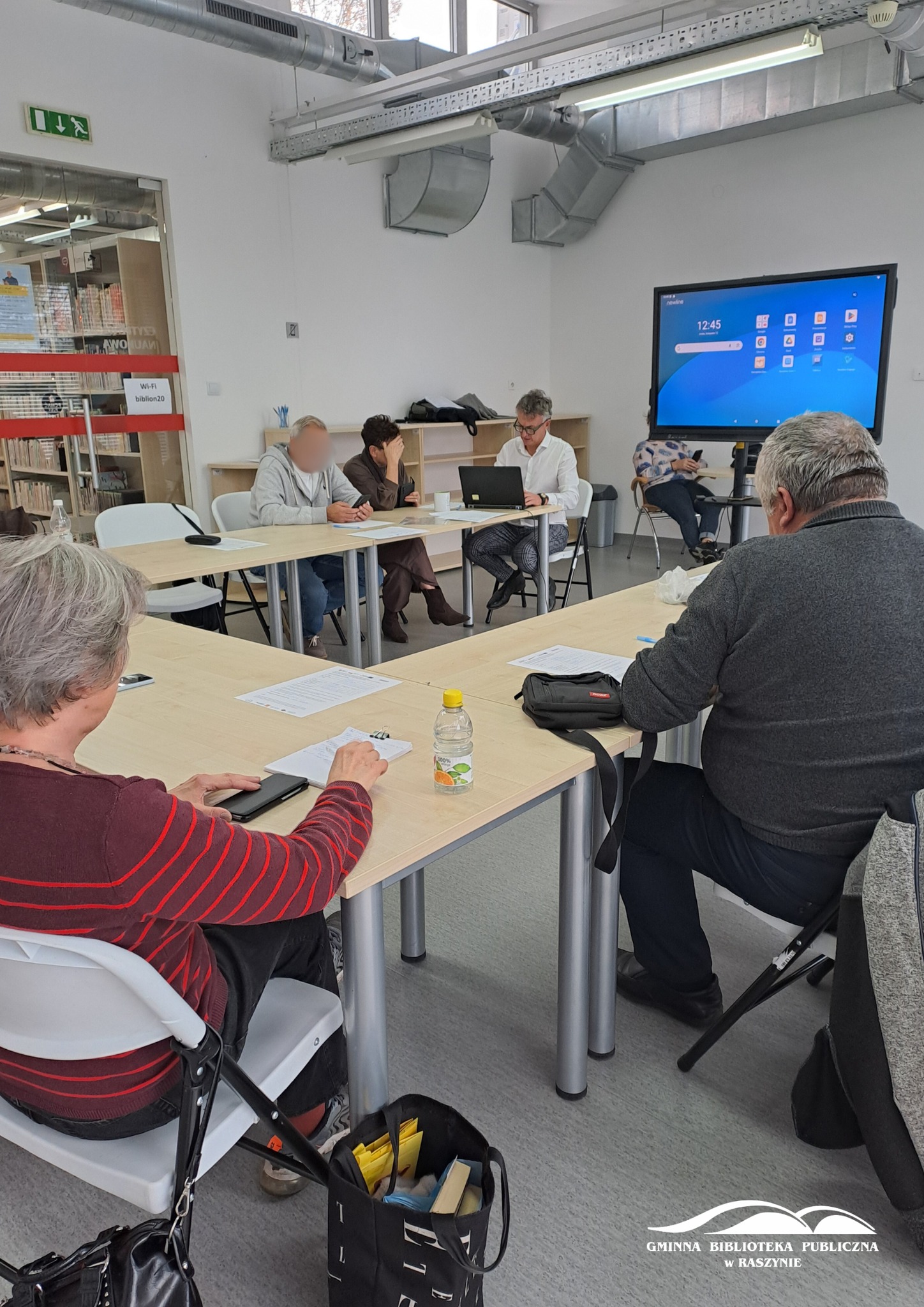 Grupa uczestników zajęć z obsługi smartfona - prowadzący tłumaczy