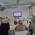 Grupa uczestników zajęć z obsługi smartfona wraz z prowadzącym, który coś tłumaczy