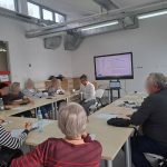 Grupa uczestników zajęć z obsługi smartfona siedzi przy stole wraz z prowadzącycm