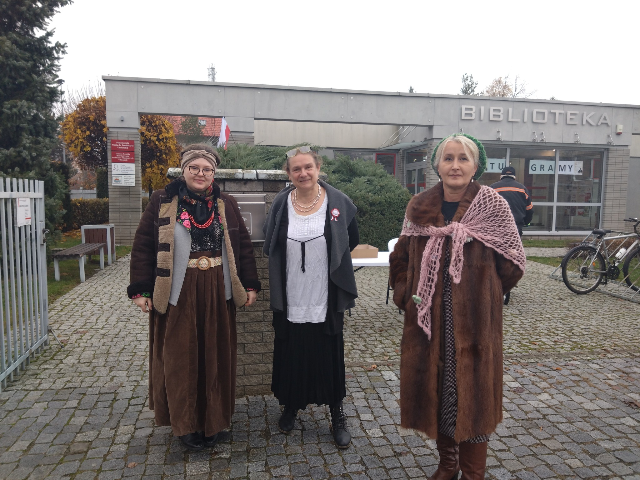 Grupa kobiet ubranych w stroje z lat międzywojennych na tle frontu biblioteki