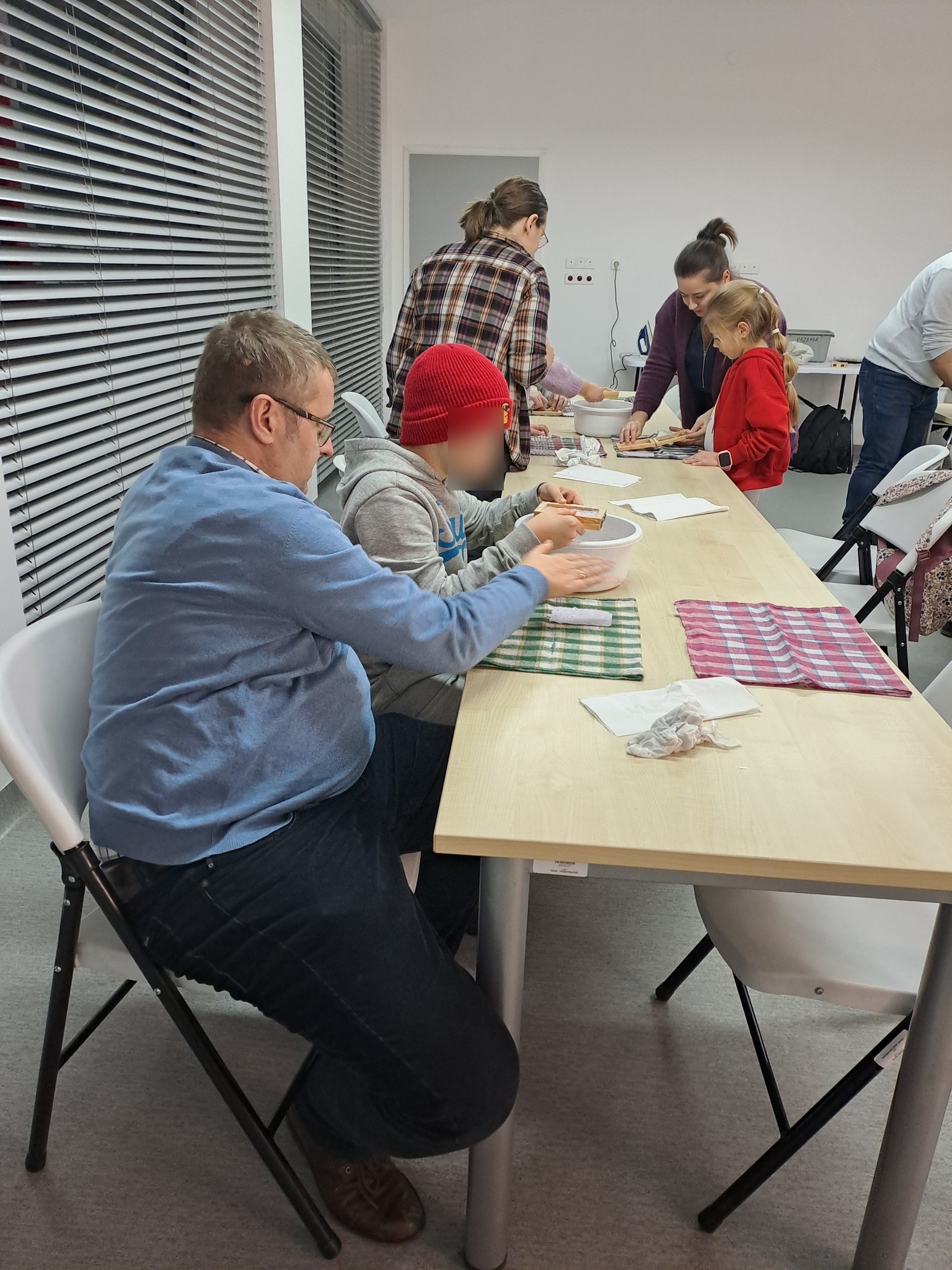 Uczestnicy przy stołach mieszają masę papierową