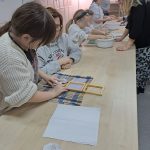 Uczestnicy przy stołach przygotowują papier czerpany