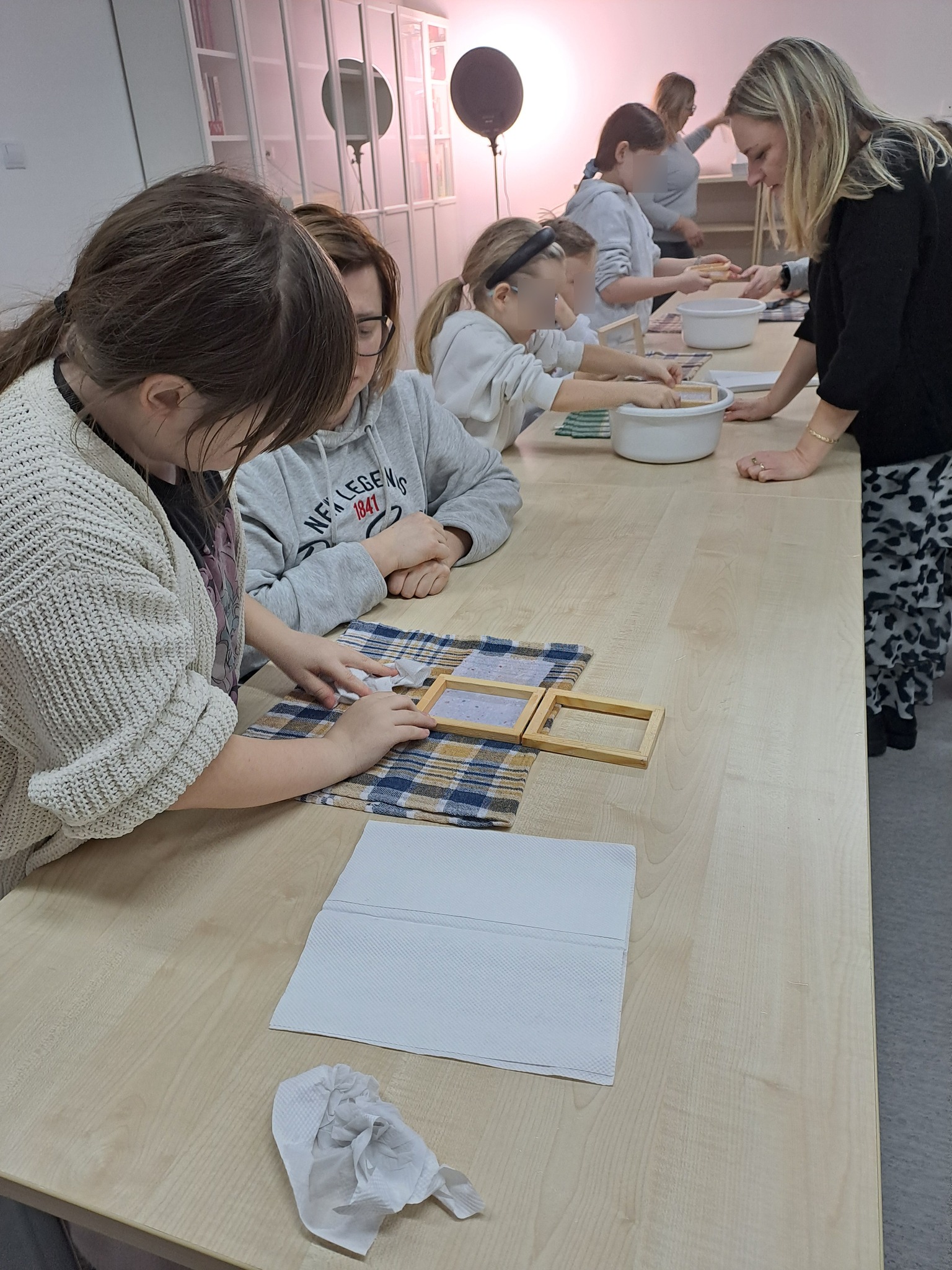 Uczestnicy przy stołach przygotowują papier czerpany