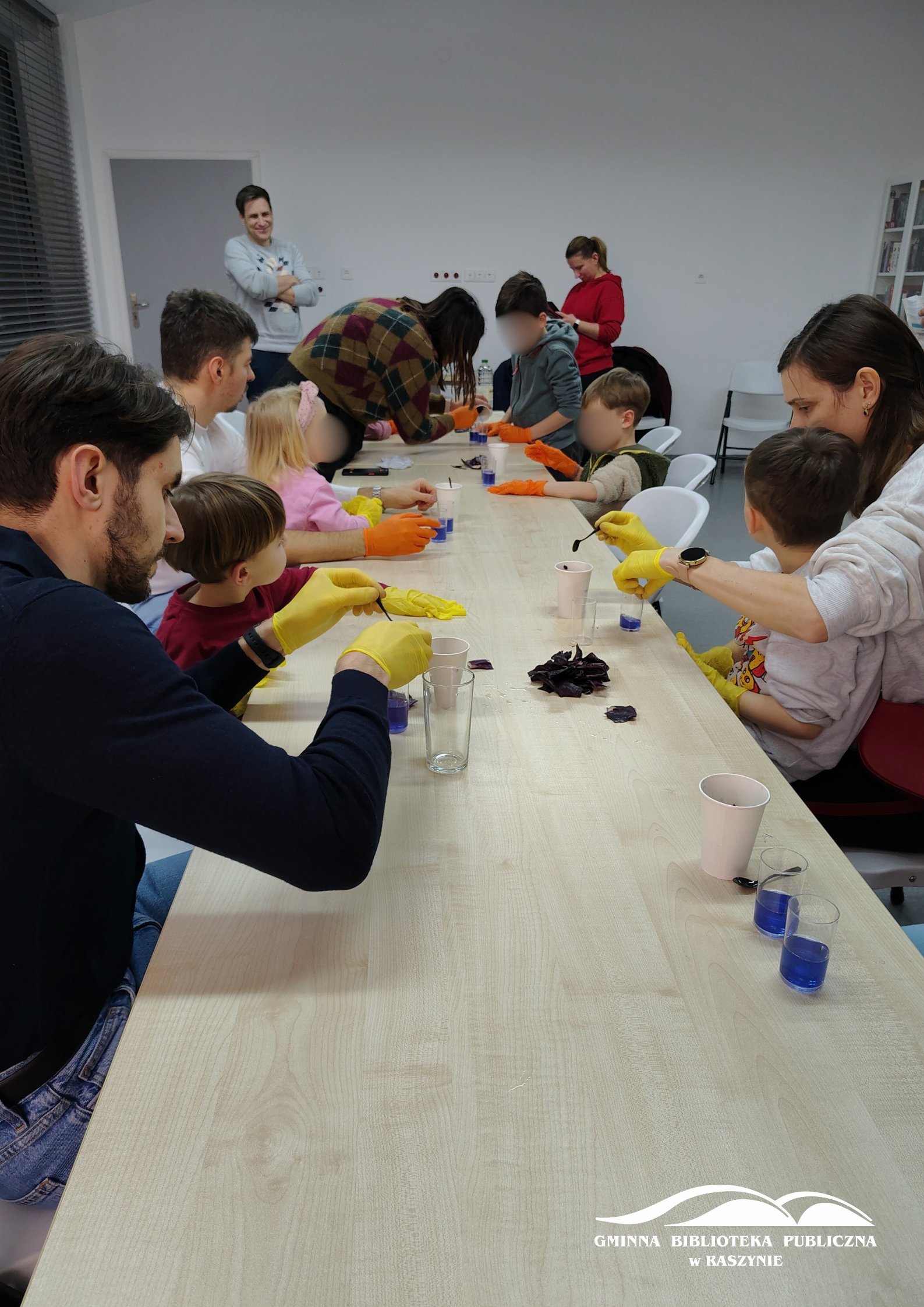 Uczestnicy siedzą wokół stołu, wlewają ocet do szklanek