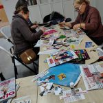 Grupa uczestników siedzi przy stołach i wycina elementy kolażu