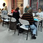 Uczestniczki siedzą przy stołach pracując nad kolażami