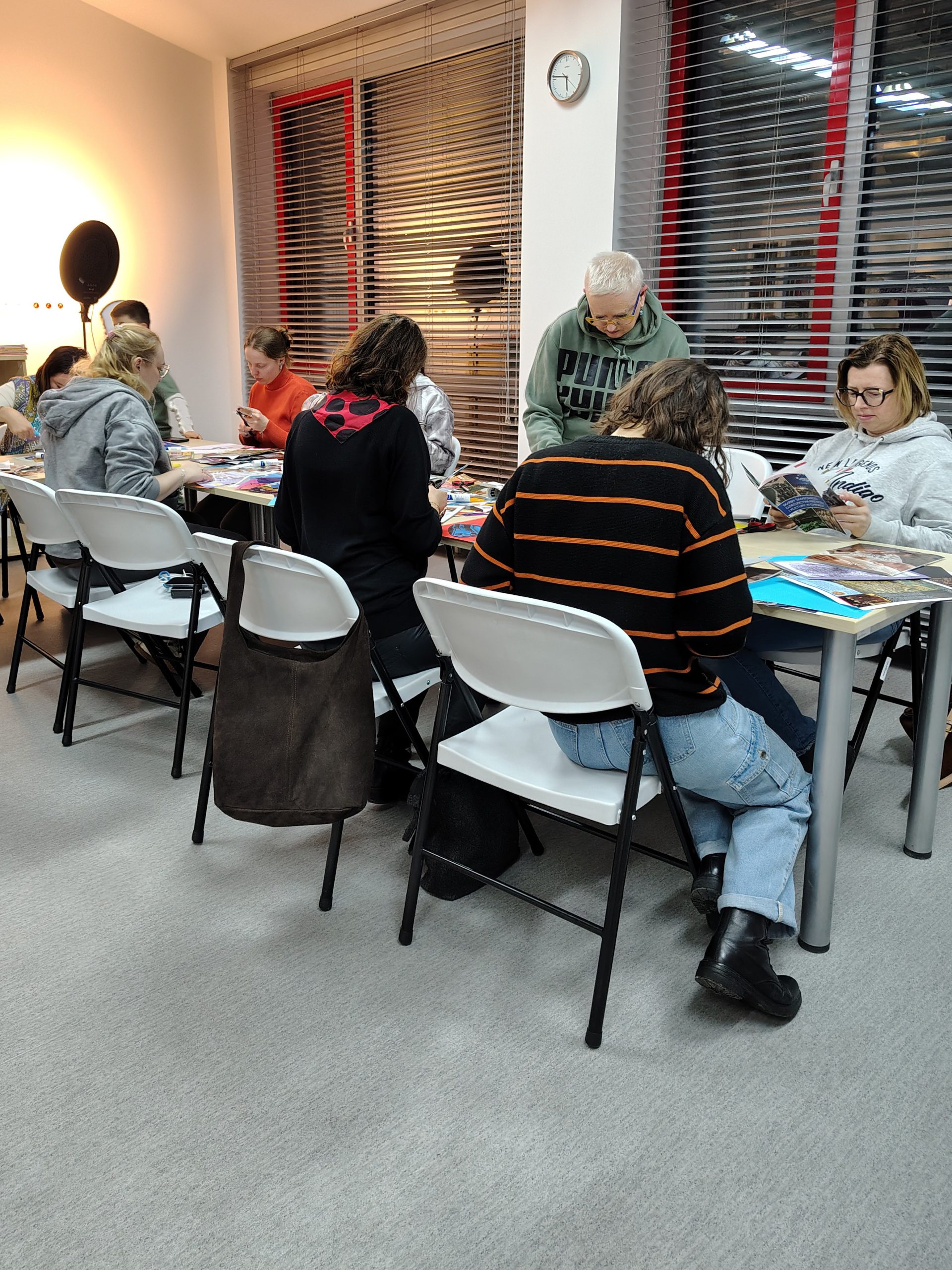Uczestniczki siedzą przy stołach pracując nad kolażami