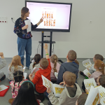 Dzieci patrzą na ekran i wspólnie z bibliotekarką rozwiązują zadanie