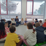 Dzieci siedzą w koło, bibliotekarka czyta książkę