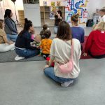 Grupa rodziców z dziećmi podczas warsztatów czytelniczych, prowadząca pokazuje ilustracje w książce