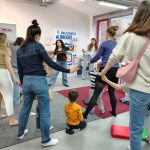 Grupa rodziców z dziećmi podczas radosnego tańca, widoczna też prowadząca zajęcia