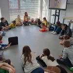 Dzieci siedzą w kole na podłodze, bibliotekarka czyta książkę