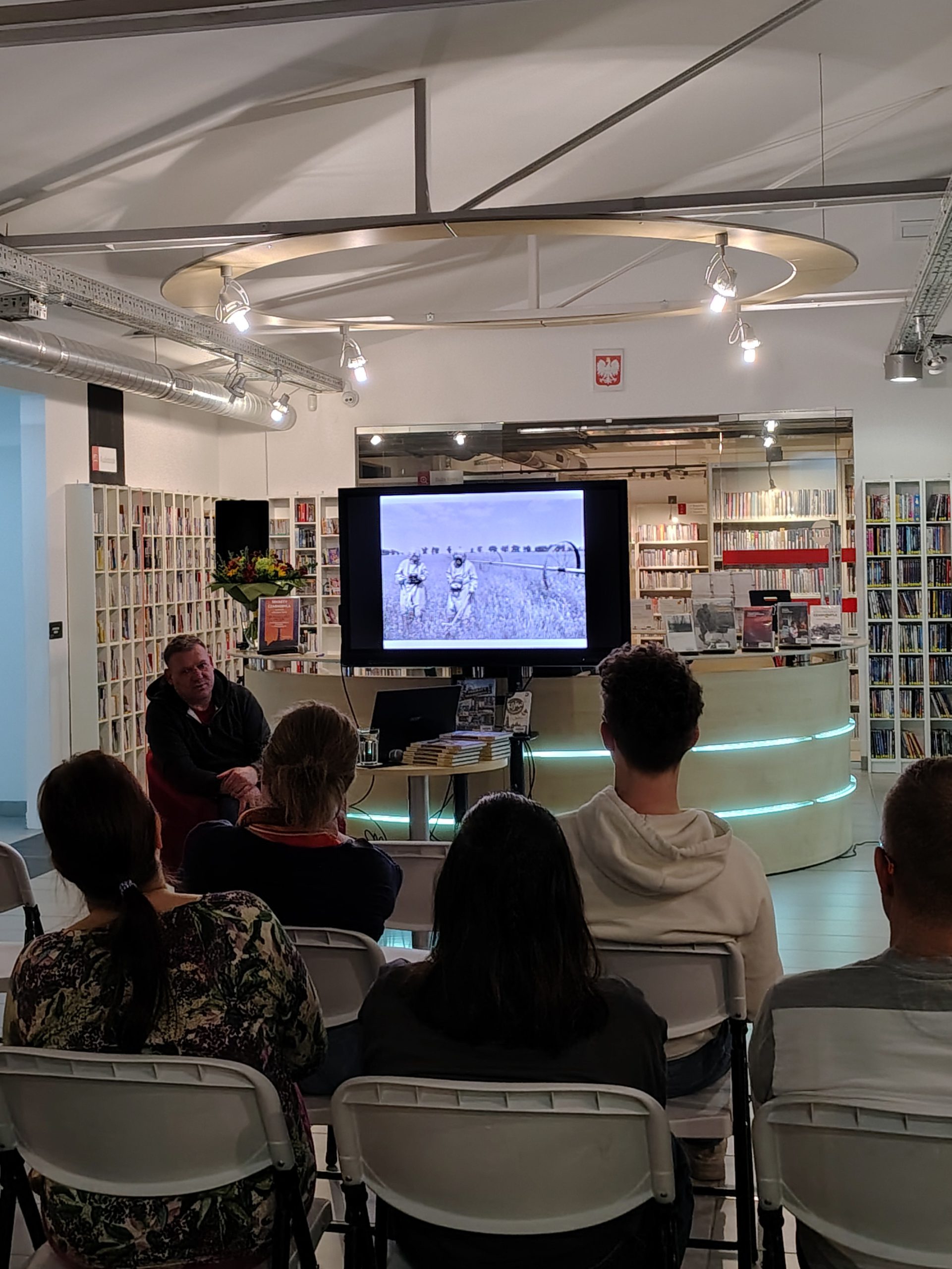 Ekran z fotografią likwidatorów podczas pracy, widoczna część publiczności