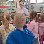 Dzieci zwiedzają bibliotekę - widoczna bibliotekarka na tle działu dla najmłodszych
