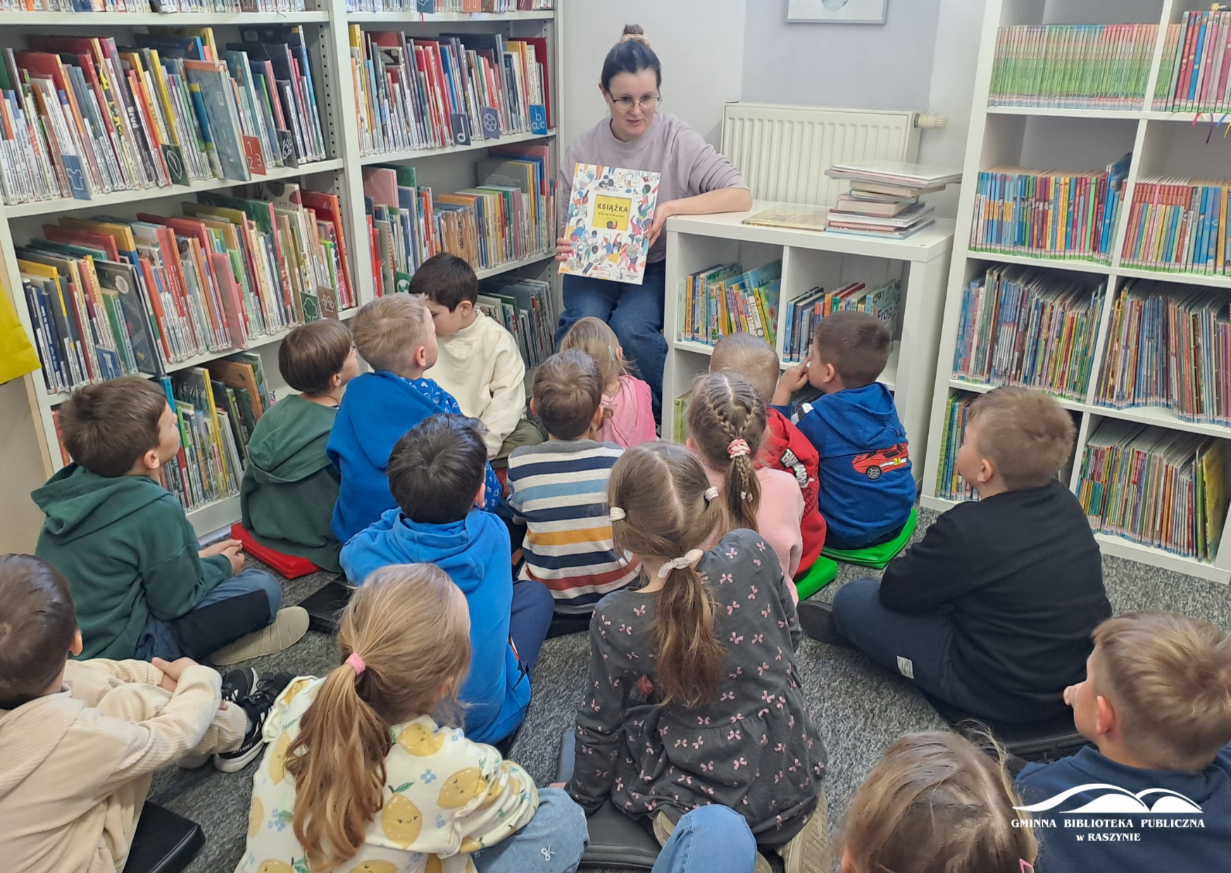 Bibliotekarka czyta książkę, dzieci siedzą na dywanie