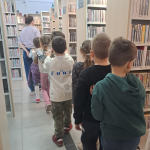 Dzieci podczas zwiedzania biblioteki - idą w rzędzie między regałami