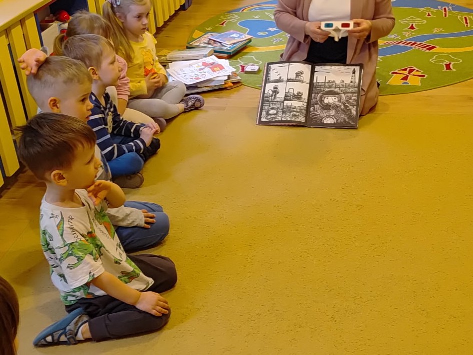 Bibliotekarka pokazuje książkę z obrazkami 3d, po lewej widoczne siedzące dzieci