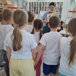 Dzieci stoją przed bibliotekarką pokazującą książkę