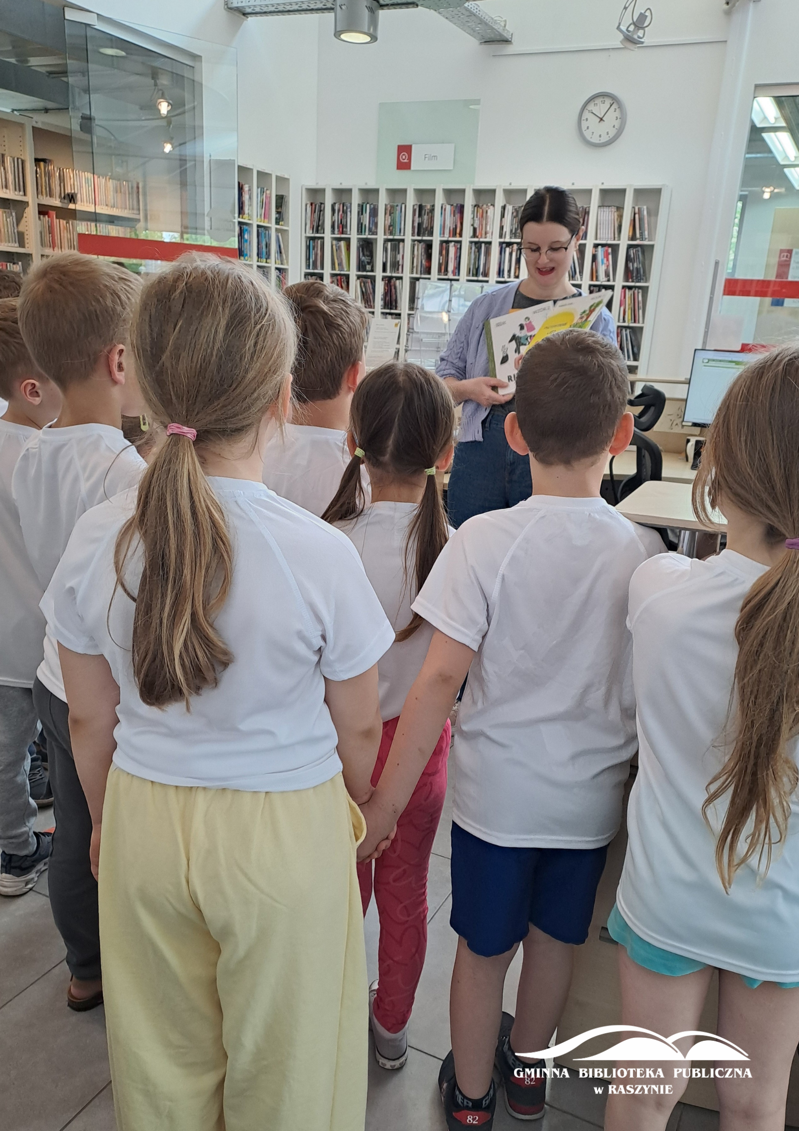 Dzieci stoją przed bibliotekarką pokazującą książkę