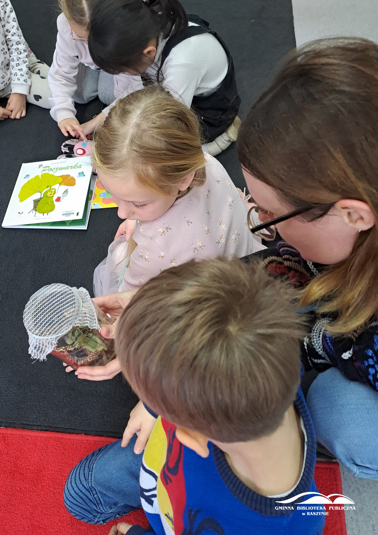 Bibliotekarka pokazuje dzieciom poczwarkę w słoiku