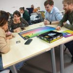 Grupa osób siedzi przy stolikach podczas gry w planszówki