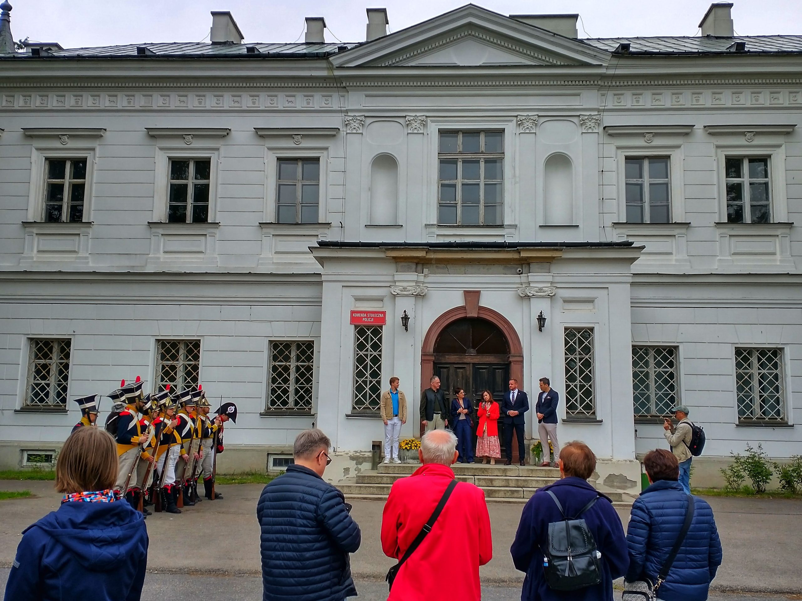 Oficjalne otwarcie pikniku - na tle drzwi pałacu w Falentach stoją m.in. prezeska Stowarzyszenia Projekt Raszyn 1809 Dorota Betko (przemawia) i starosta powiatu pruszkowskiego Adrian Ejssymont. Po lewej stoją rekonstruktorzy w mundurach z epoki