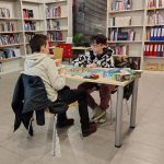 Dwóch uczestników wieczoru z grami planszowymi podczas rozgrywki przy stole w czytelni