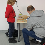 Prowadzący warsztaty pomaga w zgrzewaniu pracy żelazkiem, jeden z uczestników stoi obok