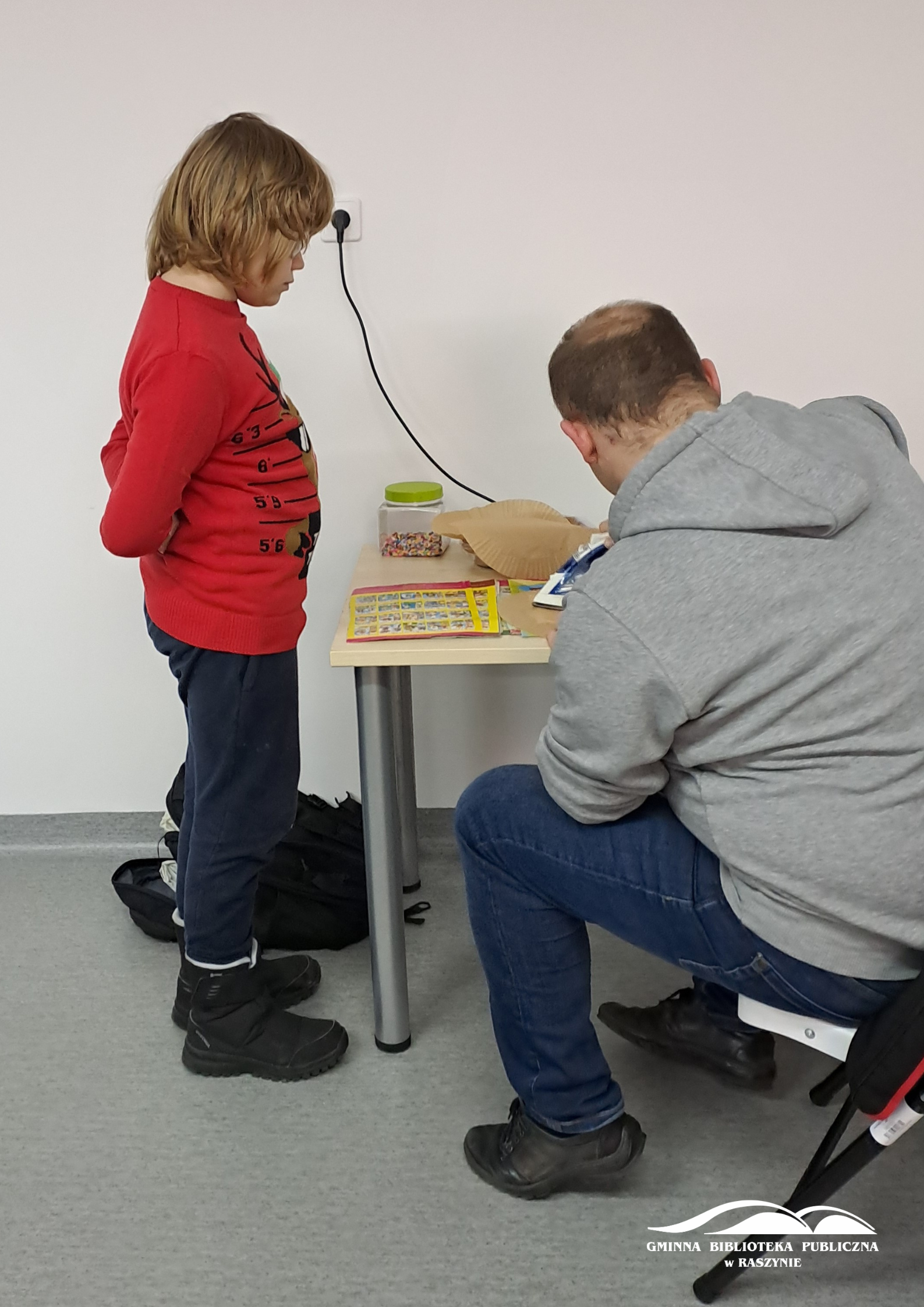 Prowadzący warsztaty pomaga w zgrzewaniu pracy żelazkiem, jeden z uczestników stoi obok