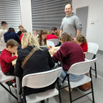 Prowadzący warsztaty wraz z siedzącymi przy stołach uczestnikami