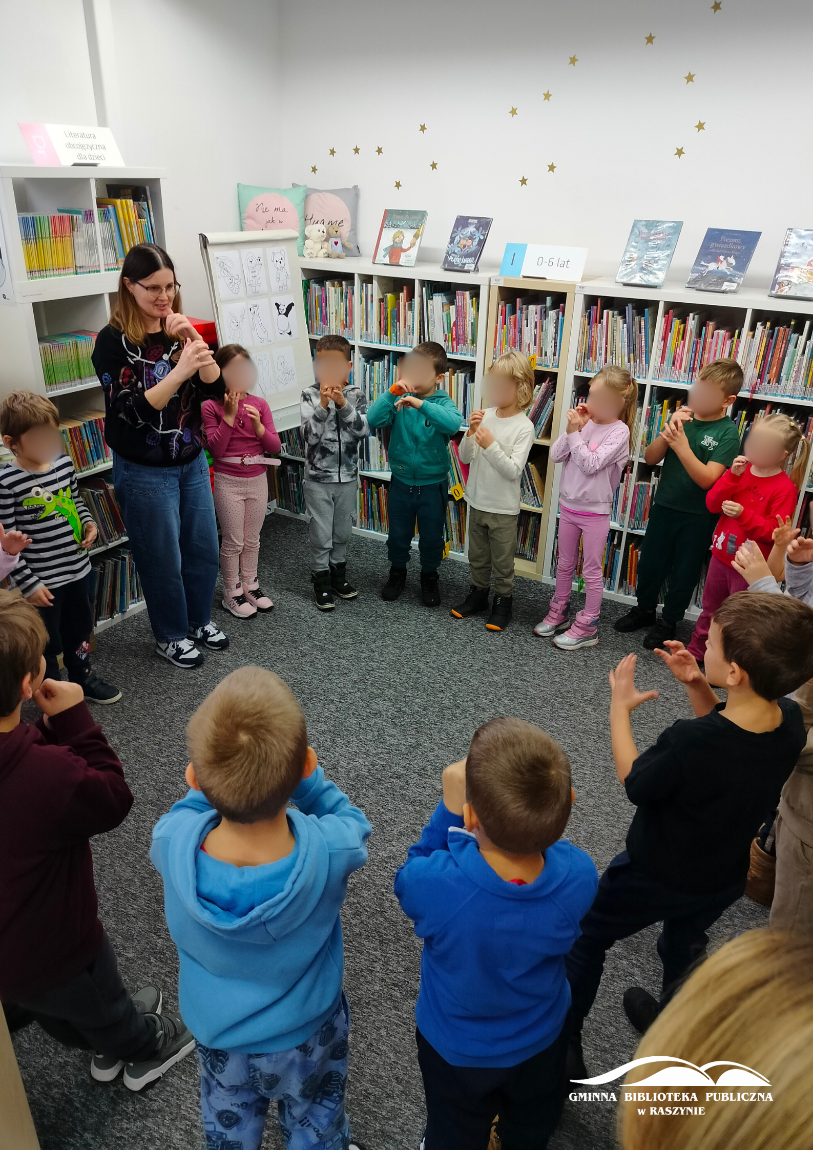Dzieci wraz z bibliotekarką ustawione w koło śpiewają misiową piosenkę