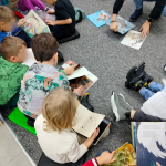 Dzieci siedzą na dywanie w dziale dla najmłodszych i oglądają książki o misiowej tematyce