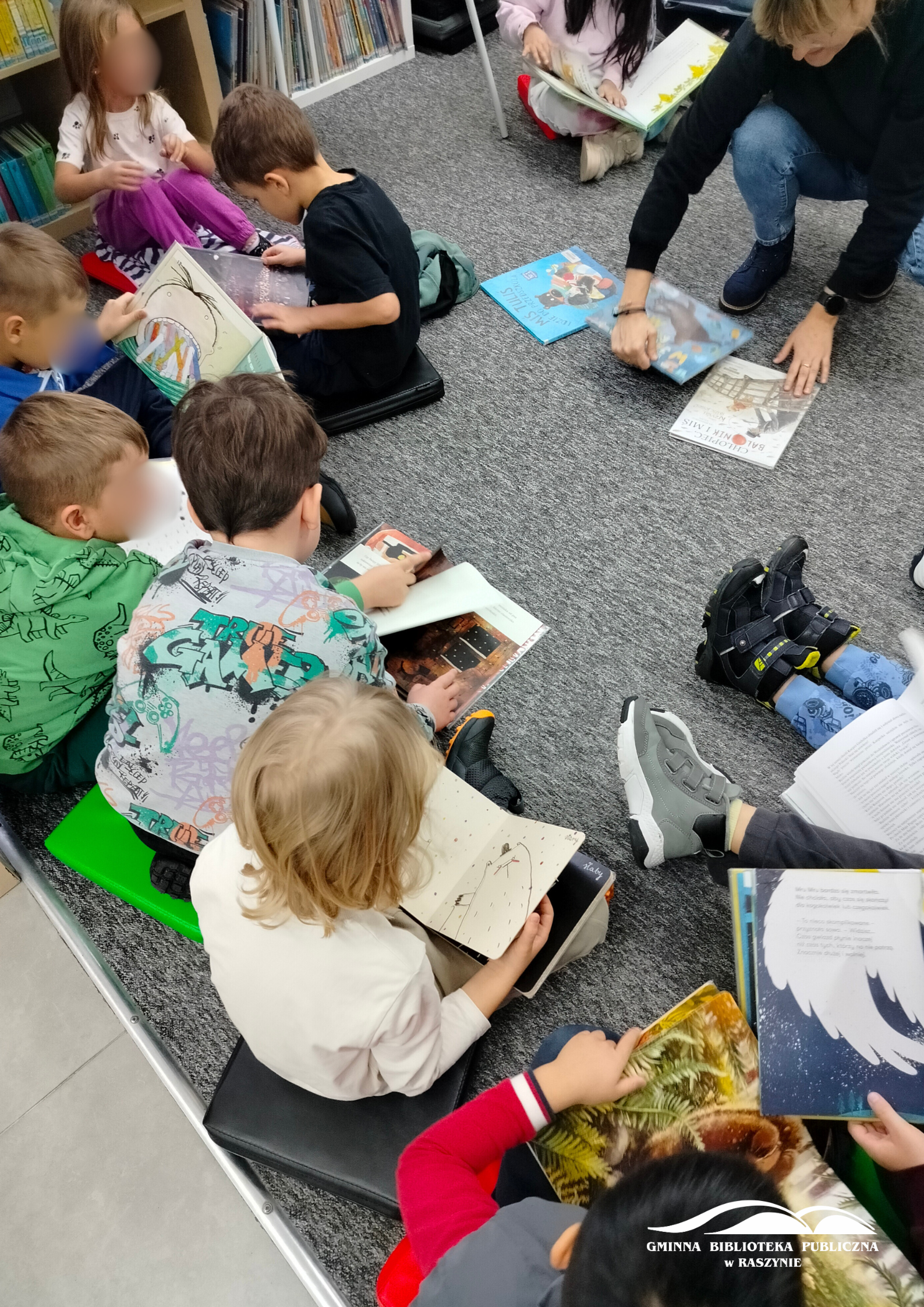 Dzieci siedzą na dywanie w dziale dla najmłodszych i oglądają książki o misiowej tematyce