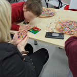 Zbliżenie na jedną z prac, uczestnik pochyla się nad nią z pęsetą