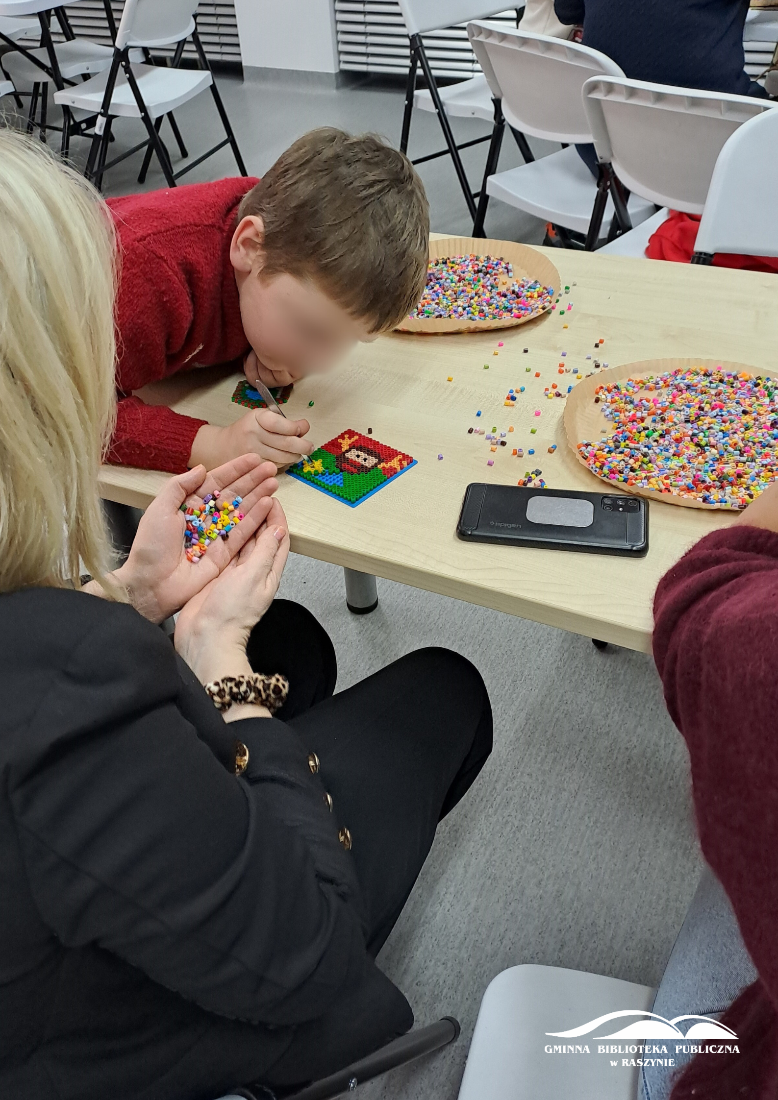 Zbliżenie na jedną z prac, uczestnik pochyla się nad nią z pęsetą
