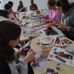 Uczestniczki warsztatów kolażowych podczas pracy - zbliżenie na stół z materiałami, widać ręce z nożyczkami