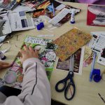 Zbliżenie na stanowisko pracy jednej z uczestniczek - widać rękę, nożyczki i powstający kolaż